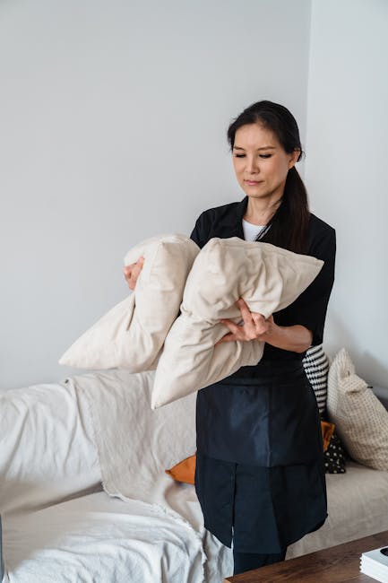 A person performing surface cleaning on a beige upholstered car seat using a handheld steam cleaning tool with a transparent nozzle, which is emitting steam onto the fabric. The seat features a textur